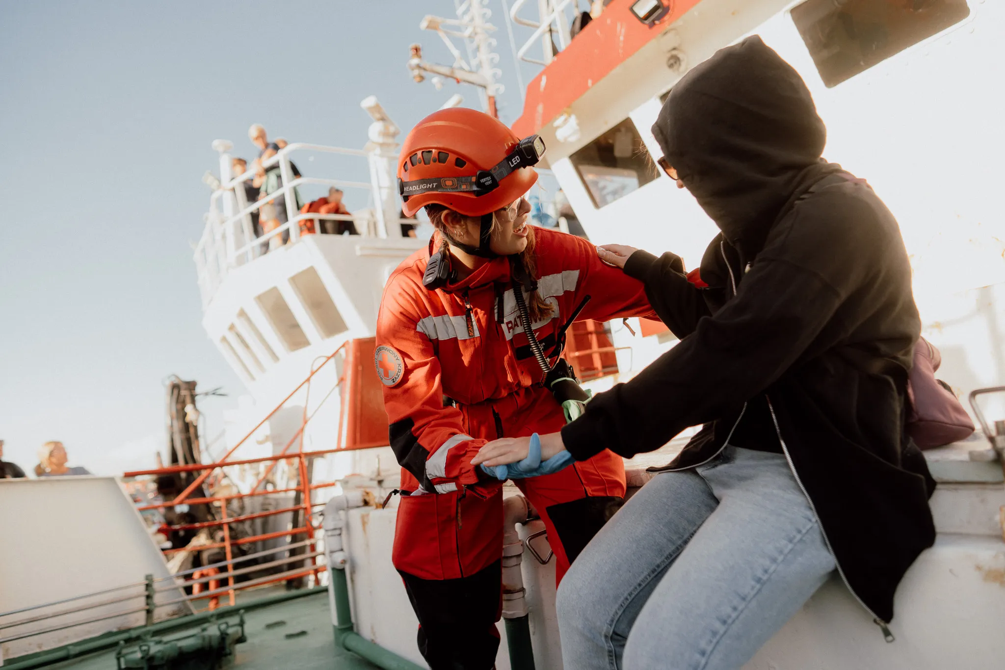 Ratowniczka PCK w czerwonym kombinezonie rozmawia z kobietą w czarnej bluzie trzymając ją za dłoń